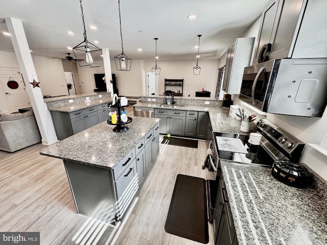 kitchen with a kitchen island, a peninsula, gray cabinets, stainless steel appliances, and light wood-style floors