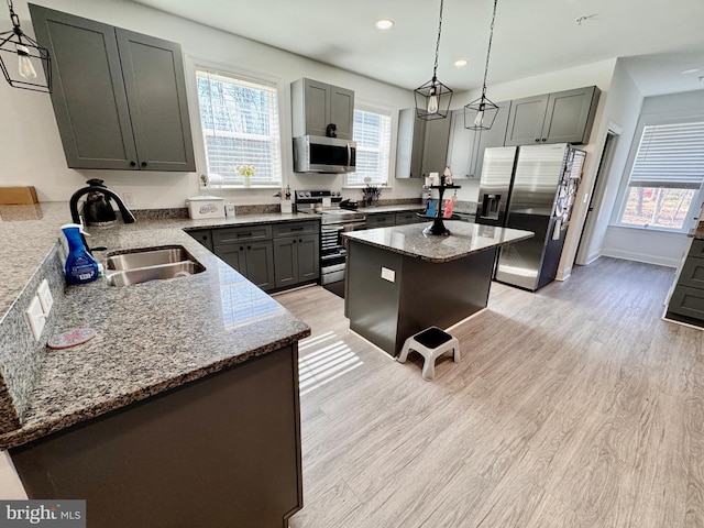 kitchen with stone counters, stainless steel appliances, a sink, light wood-type flooring, and decorative light fixtures