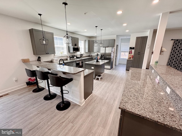 kitchen with a breakfast bar area, a peninsula, appliances with stainless steel finishes, light stone countertops, and light wood finished floors