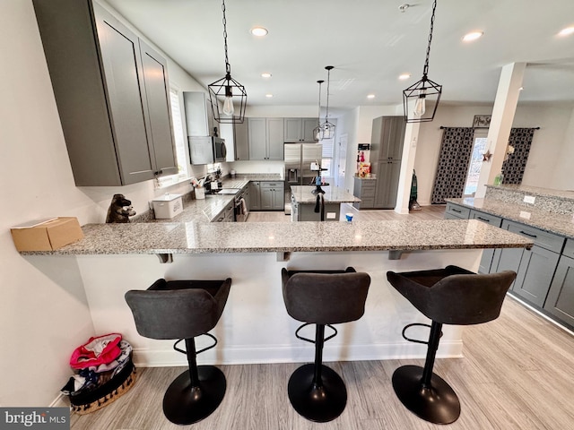 kitchen with a peninsula, appliances with stainless steel finishes, gray cabinets, and light stone countertops