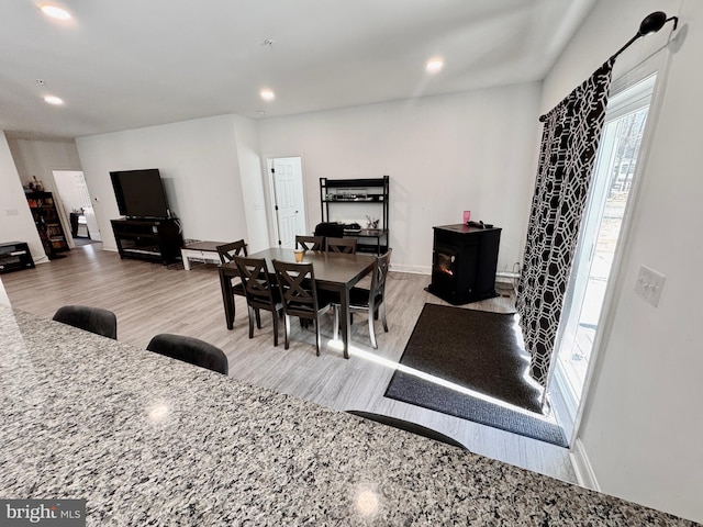 dining room featuring baseboards, wood finished floors, a wood stove, and recessed lighting