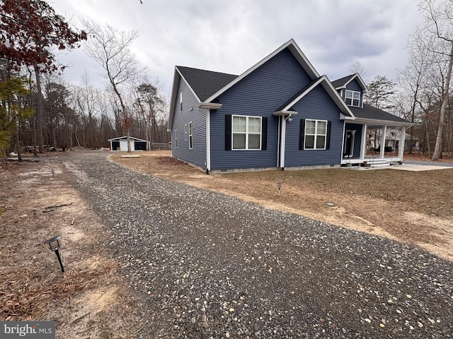 view of front of home featuring gravel driveway, covered porch, roof with shingles, and an outdoor structure