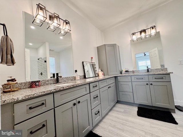 full bath with wood finished floors, a tile shower, vanity, and a healthy amount of sunlight