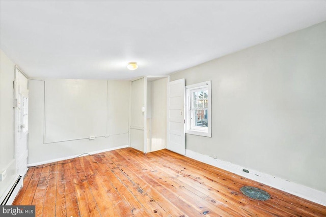 empty room featuring baseboard heating and hardwood / wood-style flooring