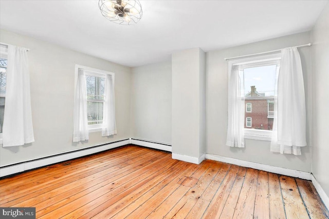 empty room featuring baseboard heating, wood-type flooring, and baseboards