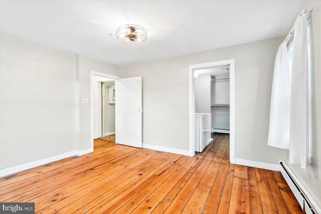 unfurnished bedroom featuring light wood-type flooring, a spacious closet, a baseboard radiator, and baseboards