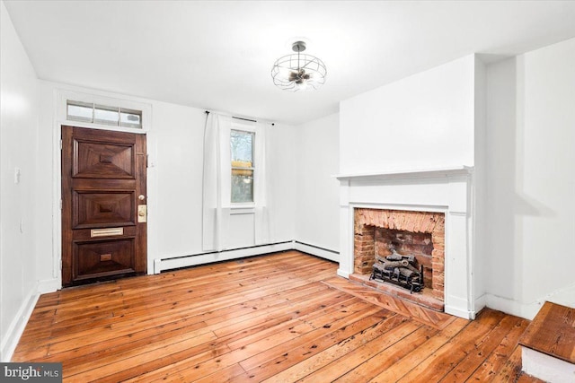 unfurnished living room featuring baseboard heating, a brick fireplace, baseboards, and hardwood / wood-style flooring