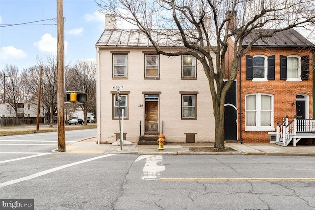 townhome / multi-family property with a standing seam roof, a chimney, and brick siding