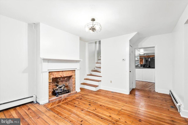 unfurnished living room featuring a fireplace, a baseboard radiator, stairway, baseboard heating, and hardwood / wood-style flooring