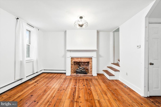 unfurnished living room with a baseboard radiator, wood-type flooring, a fireplace, and stairway