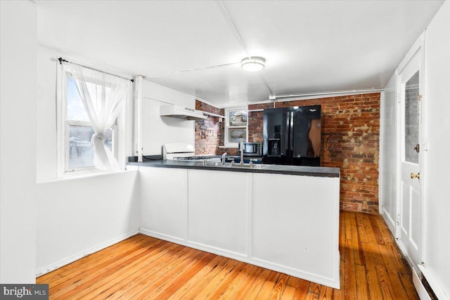 kitchen featuring dark countertops, stainless steel microwave, black fridge, brick wall, and hardwood / wood-style flooring