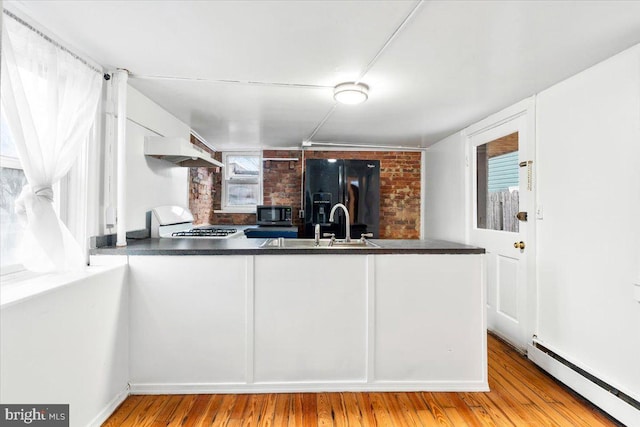 kitchen with black fridge with ice dispenser, stainless steel microwave, gas range oven, a baseboard heating unit, and a sink