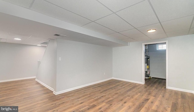 below grade area featuring visible vents, baseboards, a drop ceiling, water heater, and wood finished floors