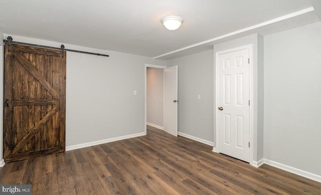 unfurnished bedroom with a barn door, baseboards, and wood finished floors