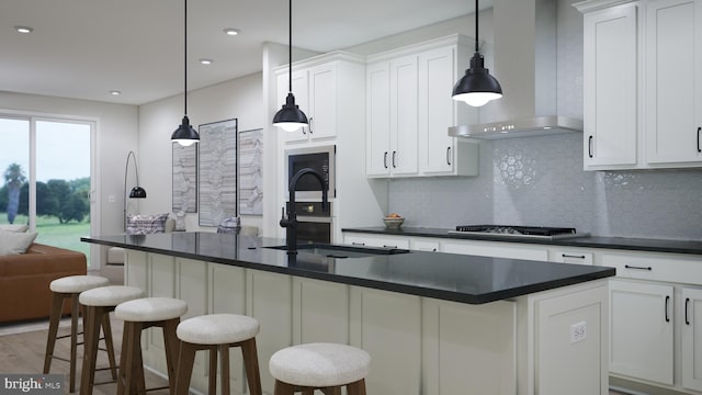 kitchen featuring dark countertops, white cabinetry, wall chimney range hood, and an island with sink