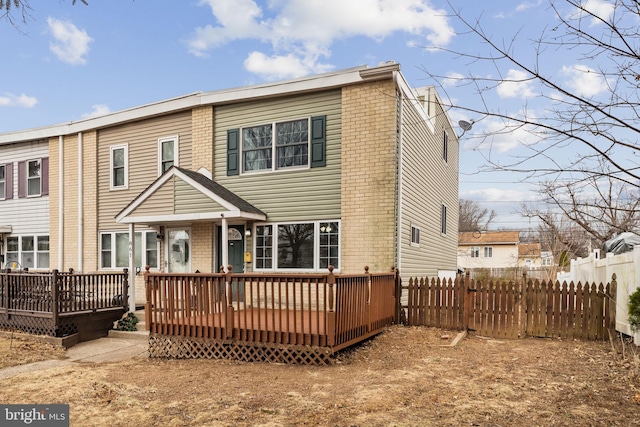 back of property with a deck, brick siding, and fence