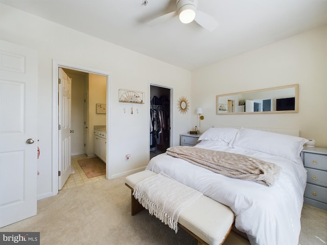 bedroom with a walk in closet, a closet, light colored carpet, ensuite bath, and baseboards