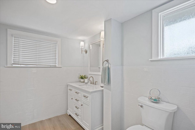 bathroom with a wainscoted wall, tile walls, toilet, vanity, and wood finished floors