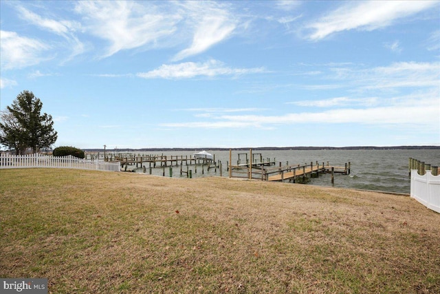 dock area with a yard, a water view, fence, and boat lift