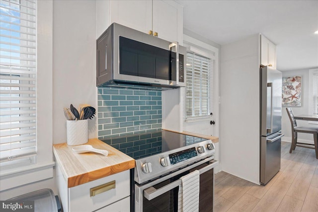 kitchen with stainless steel appliances, white cabinets, light wood finished floors, and tasteful backsplash