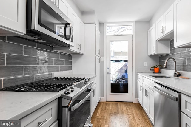 kitchen with stainless steel appliances, light wood-style floors, white cabinetry, and a sink