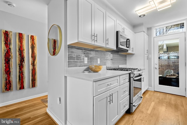 kitchen with light wood finished floors, tasteful backsplash, white cabinets, appliances with stainless steel finishes, and light countertops