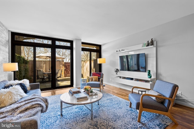 living area featuring a wall of windows, baseboards, and wood finished floors