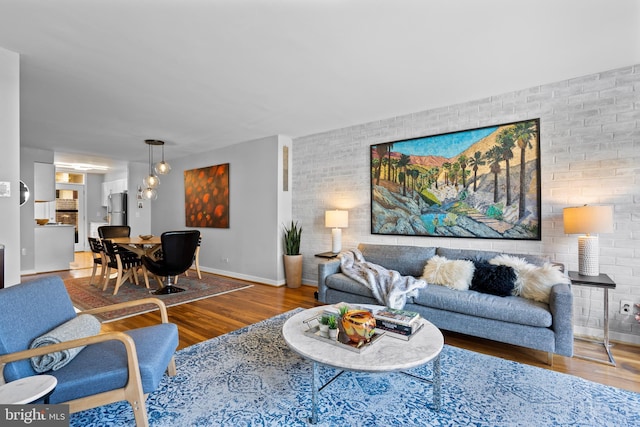 living area featuring brick wall, wood finished floors, and baseboards