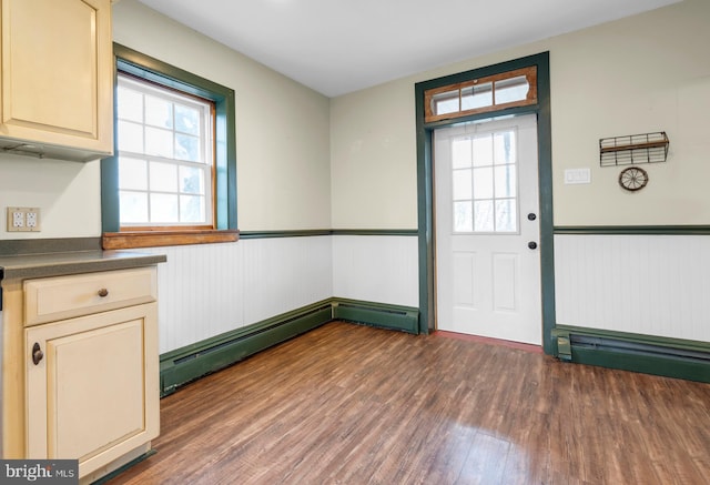 interior space with a baseboard heating unit, wainscoting, dark wood finished floors, and a wealth of natural light