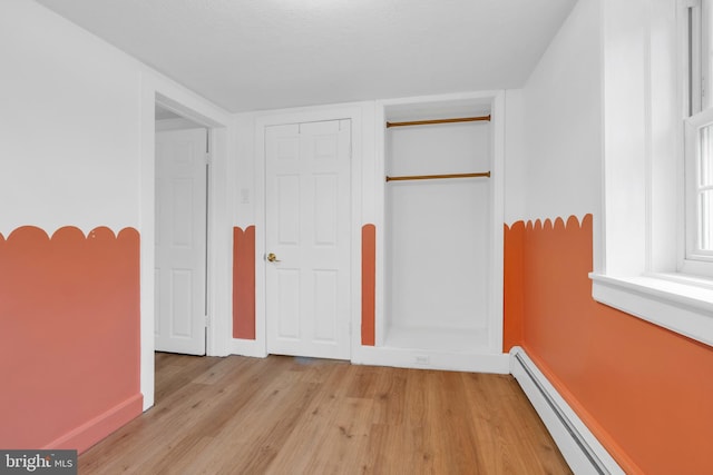 unfurnished bedroom with light wood finished floors, baseboard heating, and a closet