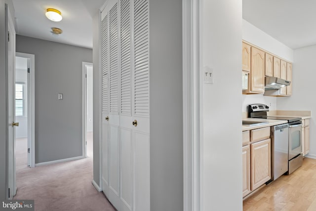 kitchen with under cabinet range hood, stainless steel appliances, baseboards, light countertops, and light brown cabinetry