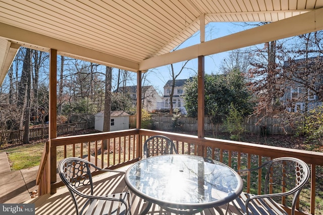 wooden terrace with outdoor dining space, a fenced backyard, a storage unit, and an outdoor structure