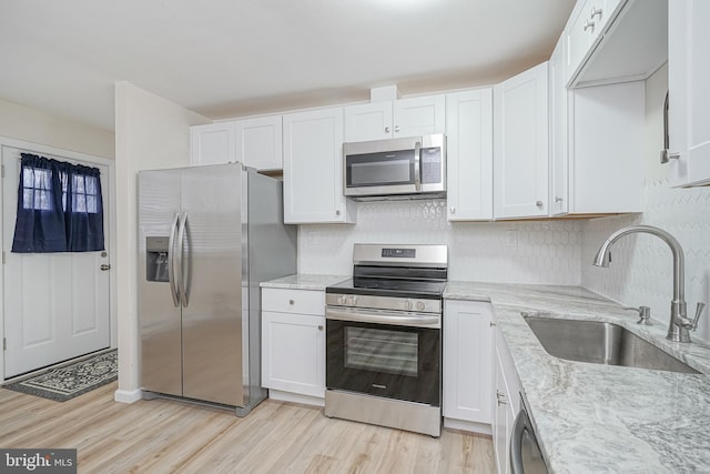 kitchen with appliances with stainless steel finishes, light wood-style floors, white cabinets, and a sink