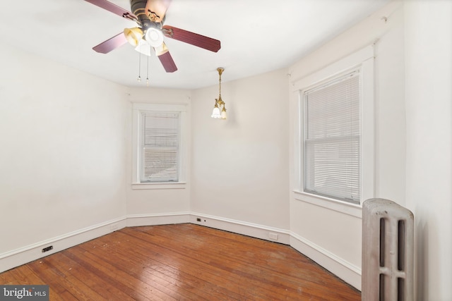 empty room featuring radiator, a ceiling fan, baseboards, and wood-type flooring