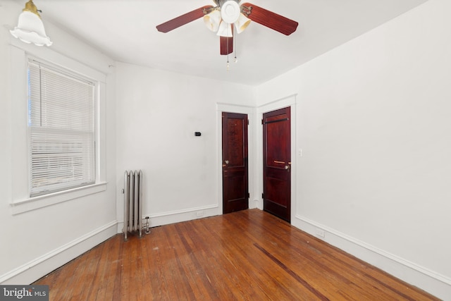 empty room with hardwood / wood-style floors, radiator heating unit, baseboards, and ceiling fan