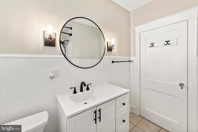 half bath featuring tile patterned flooring, toilet, vanity, and wainscoting