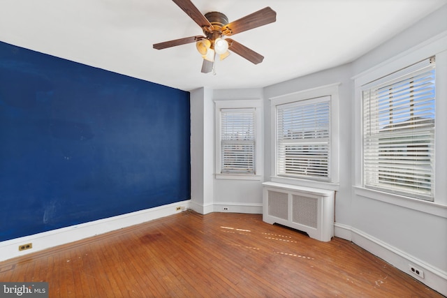 spare room with baseboards, a ceiling fan, radiator heating unit, and hardwood / wood-style flooring