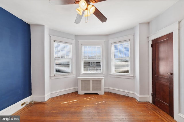 empty room with radiator, baseboards, wood-type flooring, and a wealth of natural light