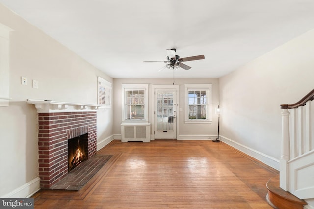 unfurnished living room featuring hardwood / wood-style flooring, radiator heating unit, stairway, baseboards, and a brick fireplace