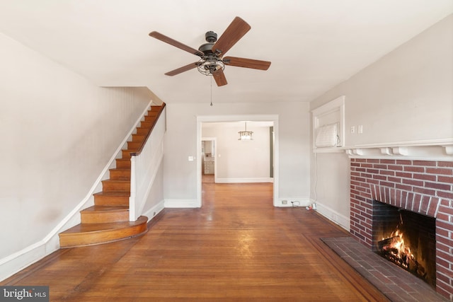 interior space featuring wood finished floors, a fireplace, baseboards, ceiling fan, and stairs