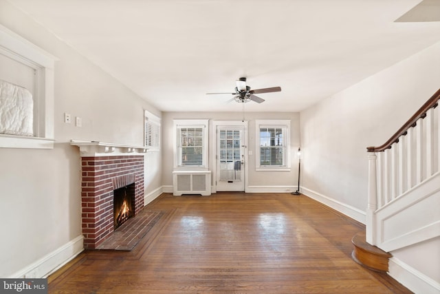 unfurnished living room with a brick fireplace, baseboards, stairway, radiator heating unit, and wood finished floors