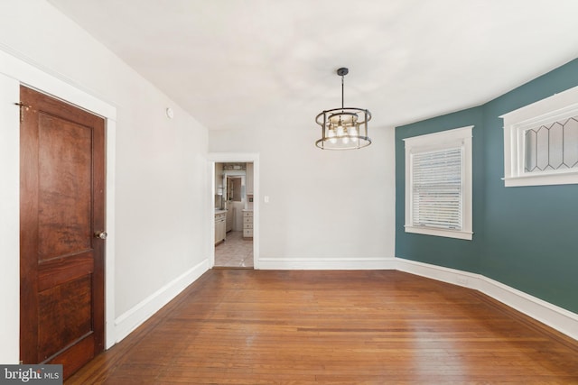 unfurnished dining area with a chandelier, baseboards, and wood finished floors