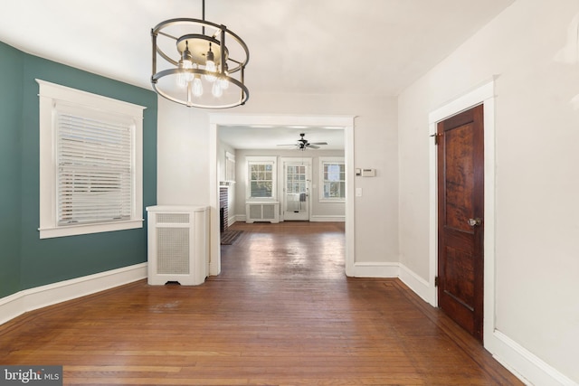 unfurnished dining area featuring ceiling fan with notable chandelier, radiator, baseboards, and hardwood / wood-style flooring