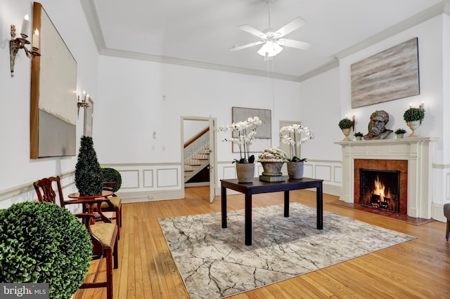 home office featuring a warm lit fireplace, light wood-style flooring, a decorative wall, ornamental molding, and wainscoting