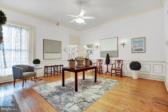 office area with crown molding, a decorative wall, a ceiling fan, wainscoting, and hardwood / wood-style flooring