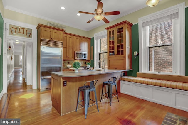 kitchen featuring brown cabinets, stainless steel appliances, light countertops, glass insert cabinets, and a kitchen bar