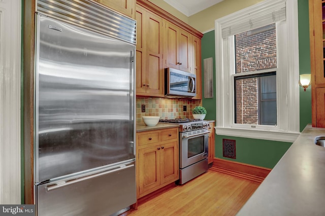 kitchen featuring light wood-style flooring, stainless steel appliances, light countertops, backsplash, and crown molding