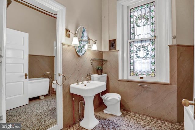 bathroom with a wealth of natural light, tile patterned flooring, a wainscoted wall, and toilet