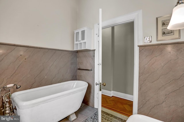 full bath featuring tile walls, a freestanding bath, and wainscoting