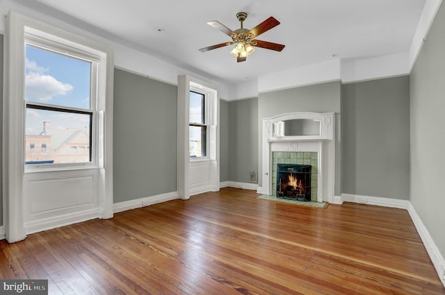 unfurnished living room with a ceiling fan, a tile fireplace, baseboards, and hardwood / wood-style floors